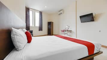 A hotel room with a bed, a desk, a chair, a TV, and an air conditioning unit.