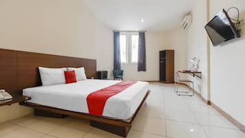 A hotel room with a large bed, a desk with a telephone, a chair, a TV mounted on the wall, and a window with curtains.