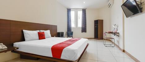 A hotel room with a large bed, a desk with a telephone, a chair, a TV mounted on the wall, and a window with curtains.