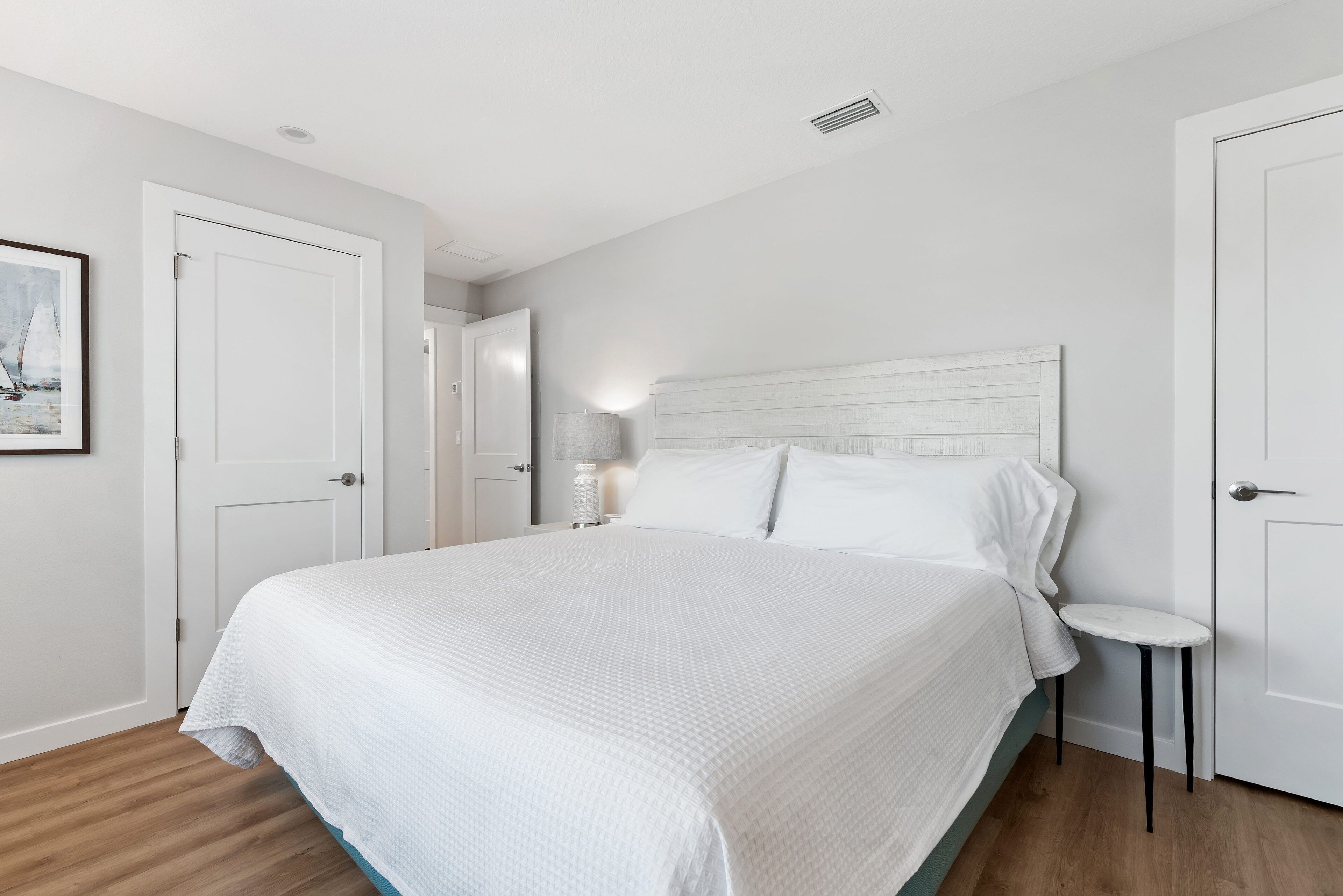 Une chambre avec un grand lit, des murs blancs et un plancher en bois.