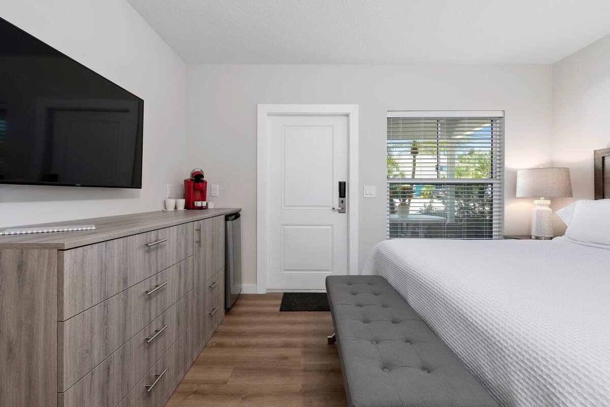 A bedroom with a bed, a TV mounted on the wall, a wardrobe, a door, and a window with blinds.