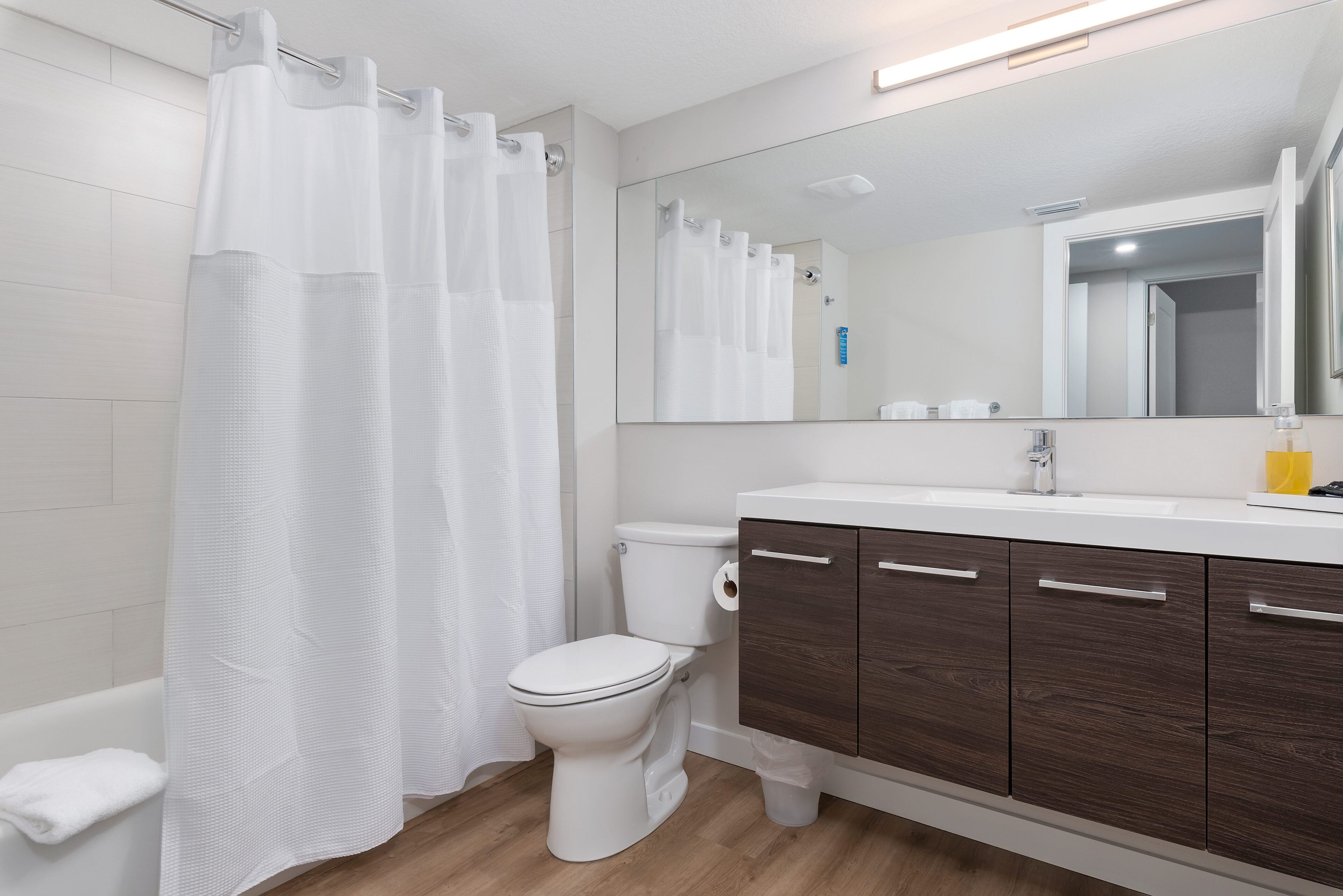 A modern bathroom with a white toilet, a shower curtain, a mirror, and wooden cabinets.