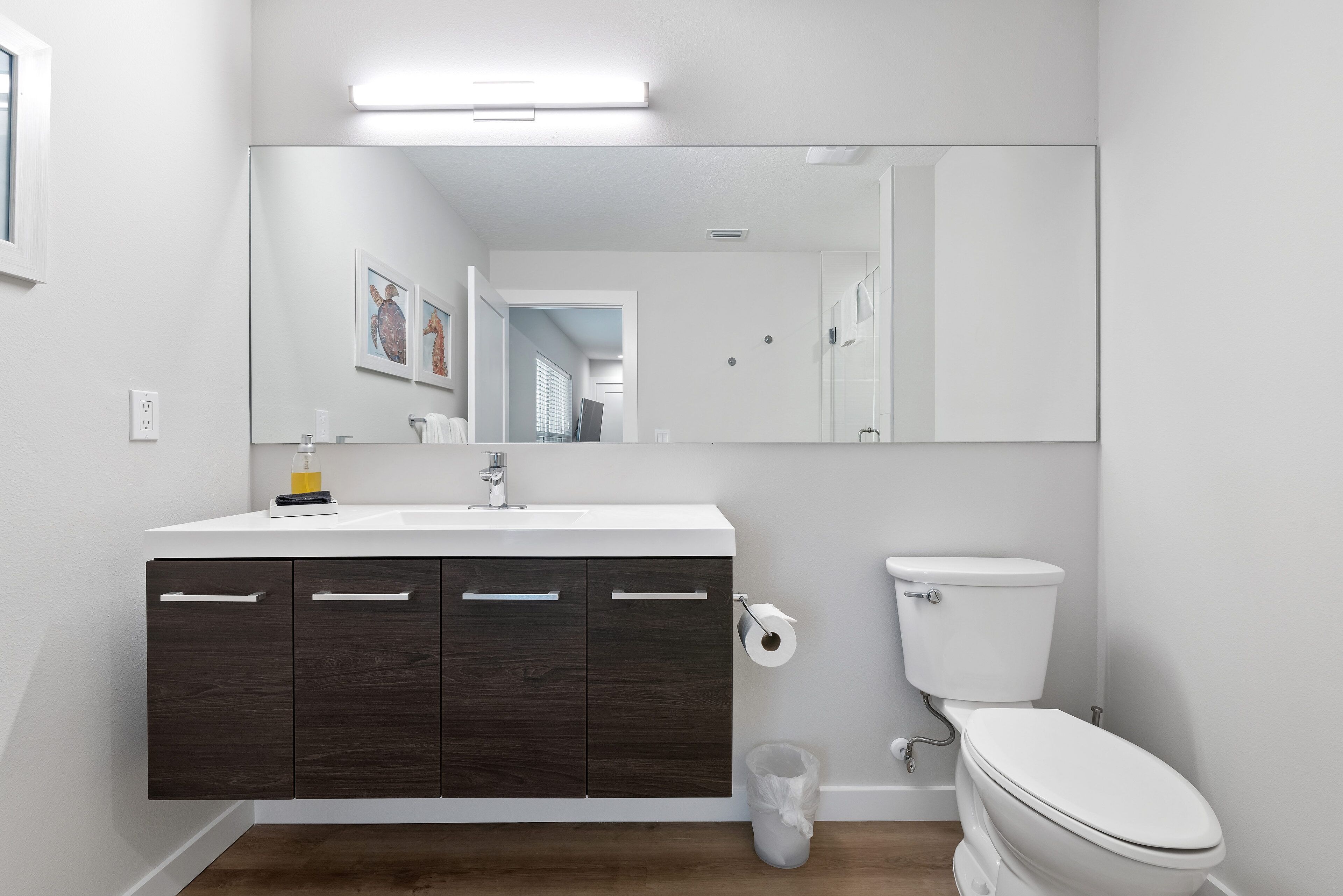 A modern bathroom with a white sink, dark wood cabinets, a toilet, and a large mirror.