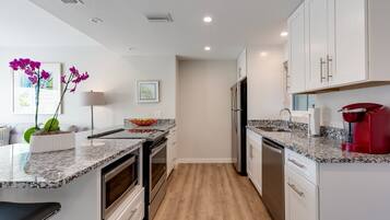 A modern kitchen with white cabinets, granite countertops, stainless steel appliances, and a wooden floor.