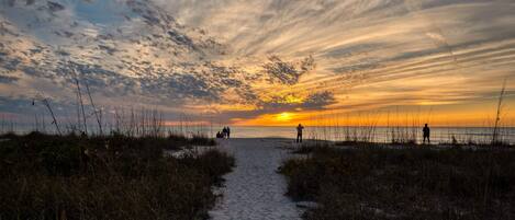 A beach path leading to the ocean with a sunset in the background.