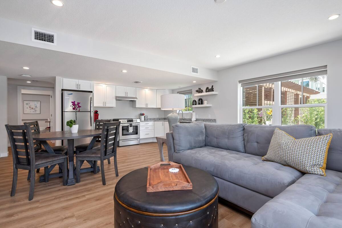 A modern living room with a grey sofa, a wooden coffee table, and a dining area with a dark wooden table and chairs.