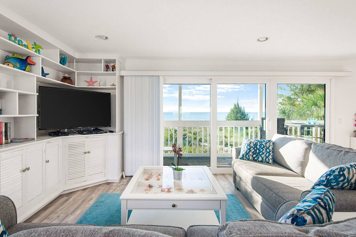 A living room with a TV, white cabinets, a sofa, and a balcony with a view.