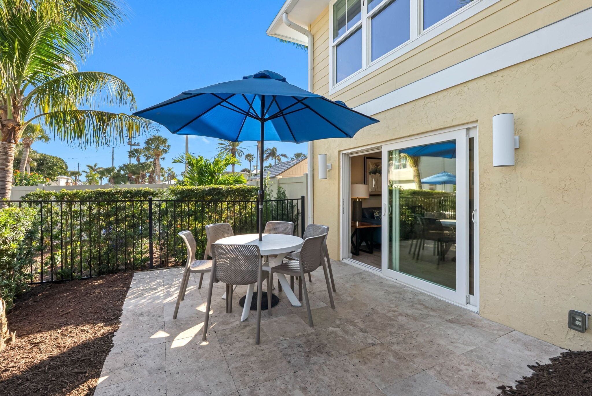A patio with a table and chairs, a blue umbrella, and a glass door leading to an indoor area.