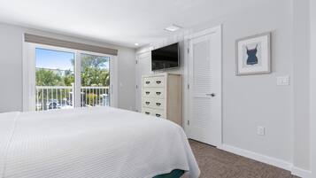 Ein Schlafzimmer mit einem großen Bett, einem an der Wand montierten Fernseher, einem Kleiderschrank und einer Glastür, die auf einen Balkon führt.