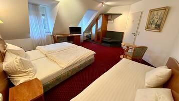 A hotel room with two beds, a desk, a television, and a small seating area.