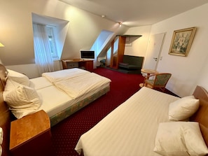 A hotel room with two beds, a desk, a television, and a small seating area.