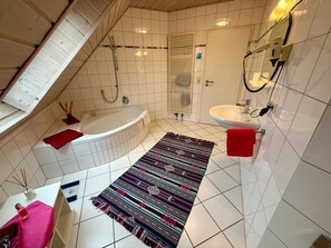 A bathroom with a bathtub, a sink, a shower, and a patterned rug.