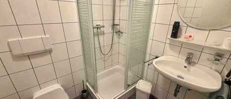 Un bagno con doccia vetrata, un water bianco, un lavandino con specchio e un pavimento piastrellato.