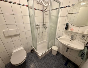 A bathroom with a glass-enclosed shower, a white toilet, a sink with a mirror, and a tiled floor.
