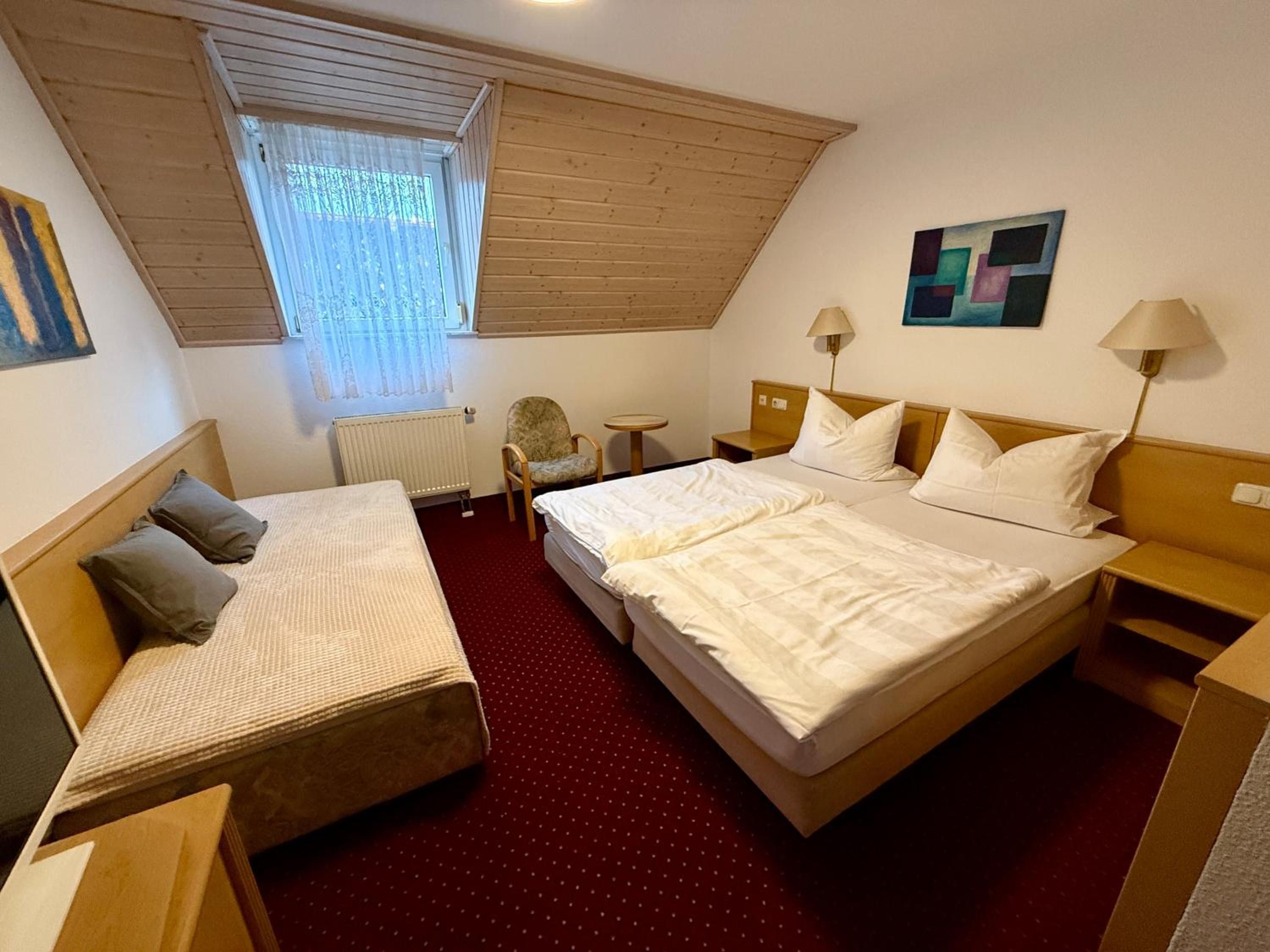 A hotel room with a large bed, a smaller bed, a desk, a chair, a radiator, and a window with blinds.