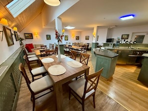 A dining area with wooden tables and chairs, a central vase with flowers, and a kitchen area with a sink and cabinets.