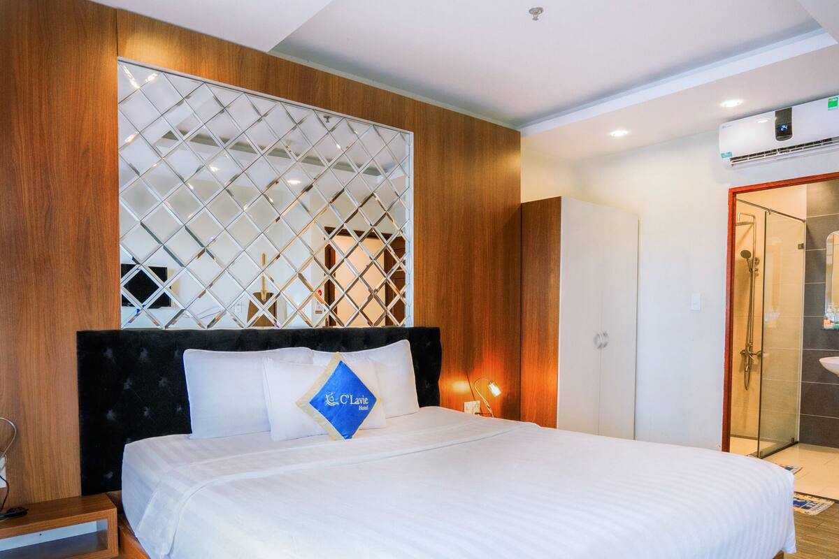 Ein modernes Hotelzimmer mit einem großen Bett, Holzvertäfelung, einer Wanddekoration und einem sichtbaren Badezimmer mit einer Glasdusche.