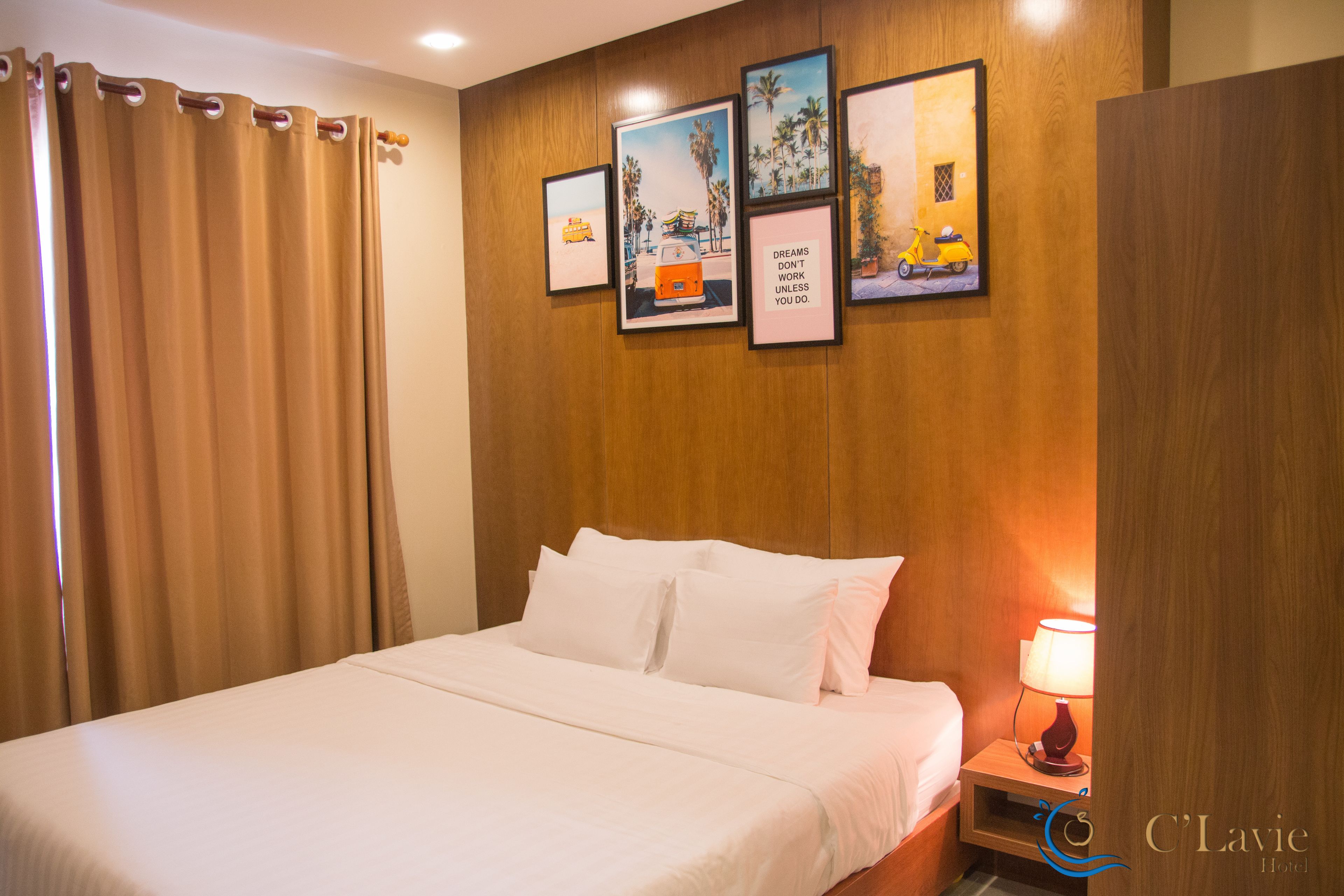A hotel room with a bed, a nightstand with a lamp, and three framed pictures on the wall.