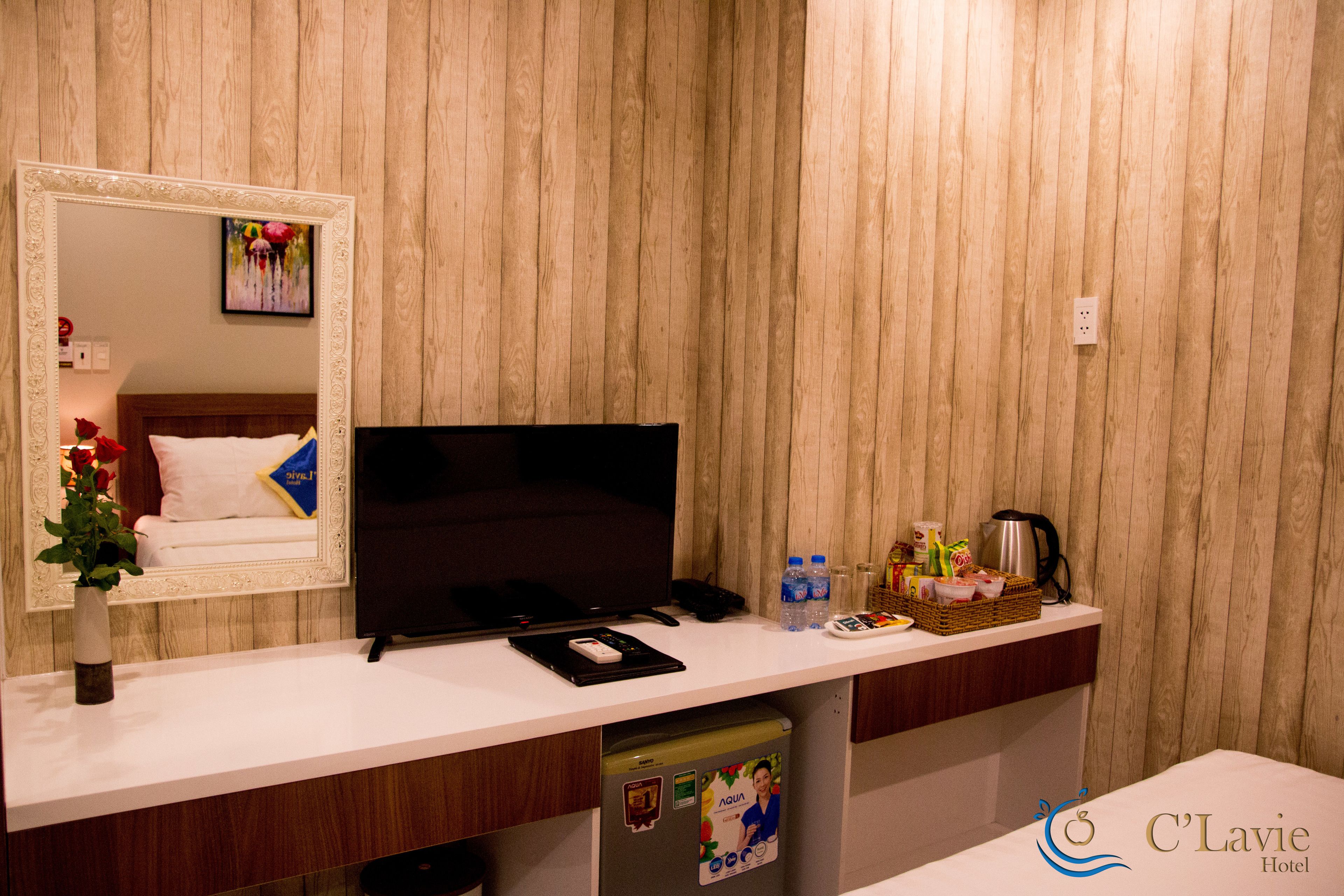 A hotel room with a wooden panel wall, a large mirror, a flat-screen TV, a small refrigerator, a coffee maker, and a basket of toiletries.