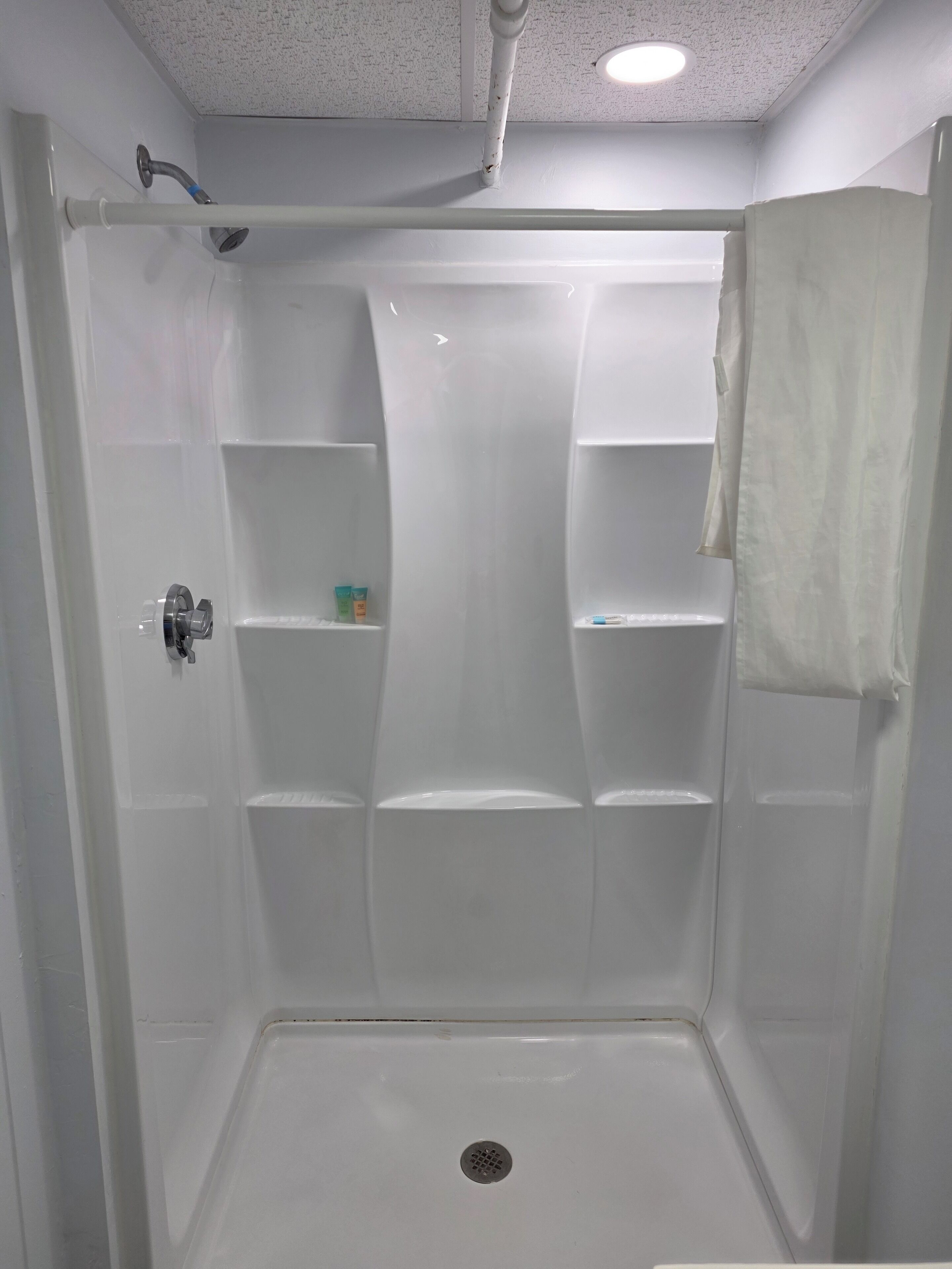 A white walk-in shower with a glass door, a showerhead, and a towel rack.