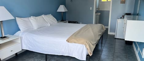 Un dormitorio con una cama, mesitas de noche, un aparador y una puerta que da al baño.