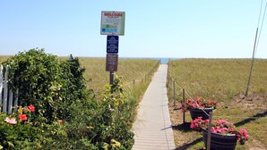 A pathway leading to a beach with a welcome sign, a no smoking sign, and potted flowers along the sides. - Seagrass Inn (Old Orchard Beach)