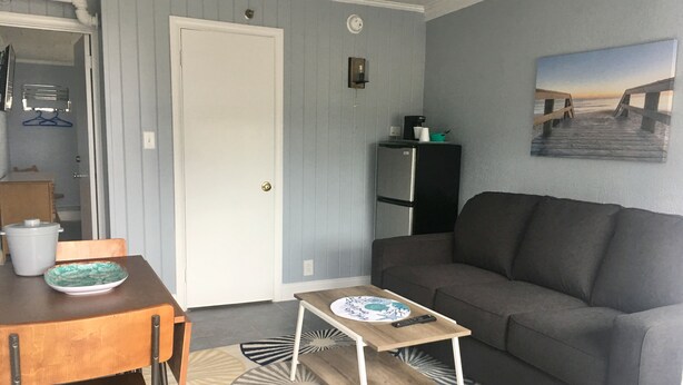 A compact living space with a grey sofa, a small wooden table, and a patterned rug. - Seagrass Inn (Old Orchard Beach)
