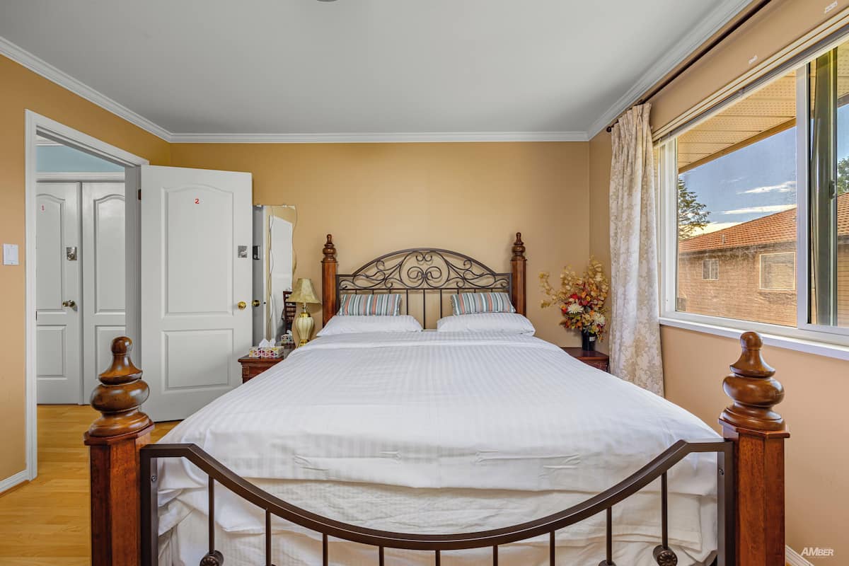 A bedroom with a large bed, wooden headboard, and a window with curtains.
