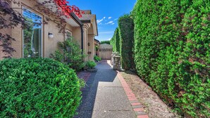 A residential pathway flanked by lush greenery and a house with a visible garage door. - Charming Family Hotel (Richmond)
