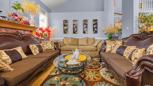 A spacious living room with a brown leather sofa set, a glass coffee table, and a variety of decorative items including flowers and wall art. - Charming Family Hotel (Richmond)