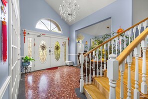 A spacious hallway with a wooden staircase, a chandelier, and a door with decorative glass panels. - Charming Family Hotel (Richmond)