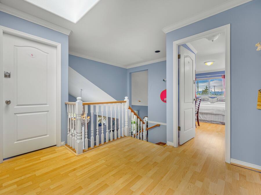 A hallway with a wooden floor, a white door, and a staircase with white railings.