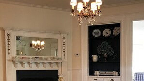 A dining room with a round table, black leather chairs, a chandelier, a fireplace, and a mirror above it. - The Belmont Inn (Camden)