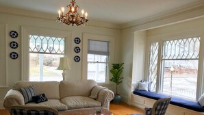 A living room with a beige sofa, checkered chairs, a coffee table, and a chandelier. - The Belmont Inn (Camden)