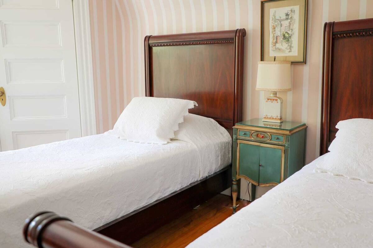 Ein Hotelzimmer mit zwei hölzernen Betten, einem Nachttisch im Vintage-Stil und einem gerahmten Bild an der Wand.
