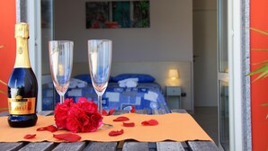 A room with a bed, a nightstand, a bottle of champagne, two glasses, and red flowers on a table. - B&B Zefiro (Pompei)
