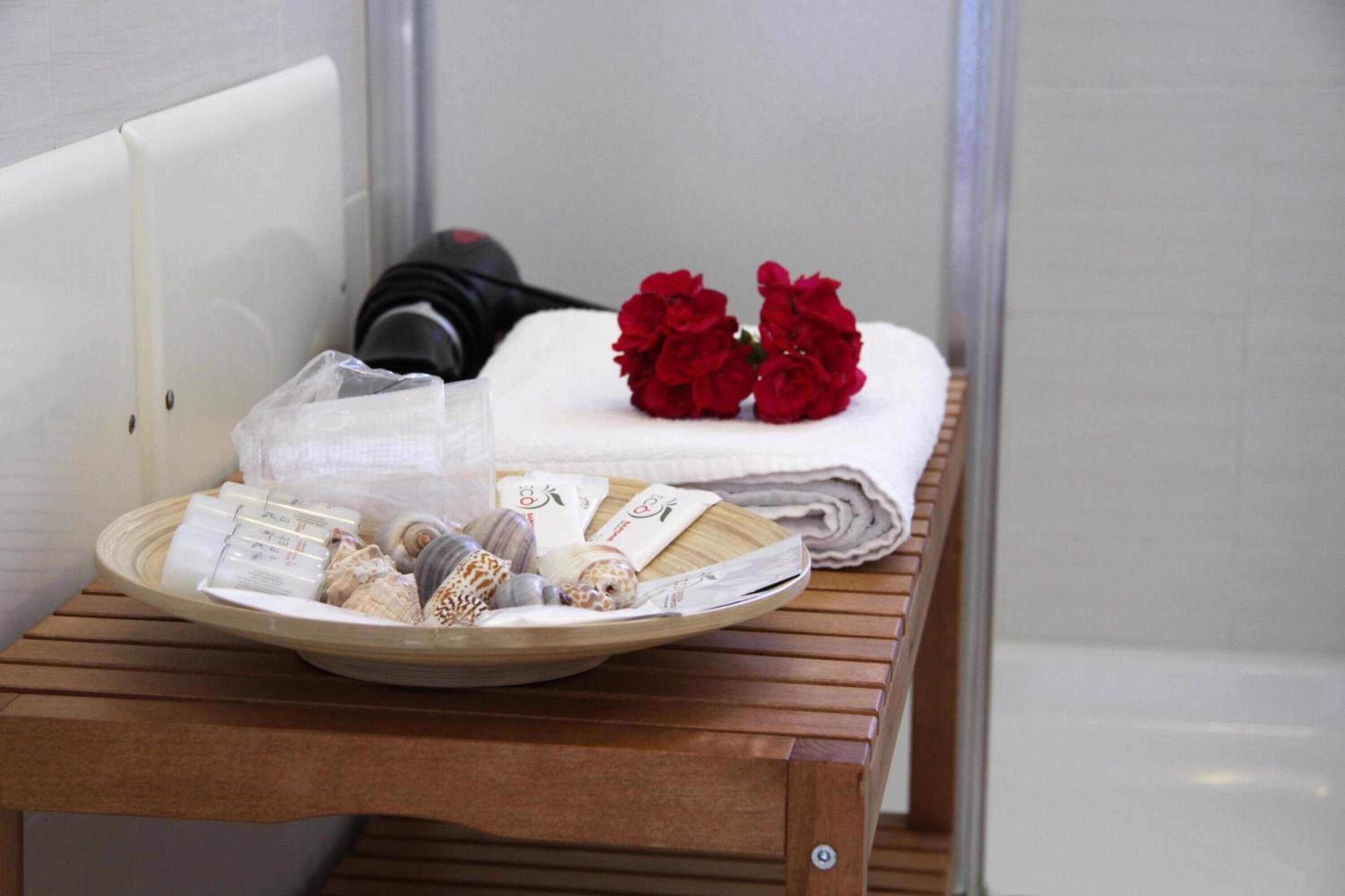 A bathroom with a wooden bench, a towel, and red flowers.