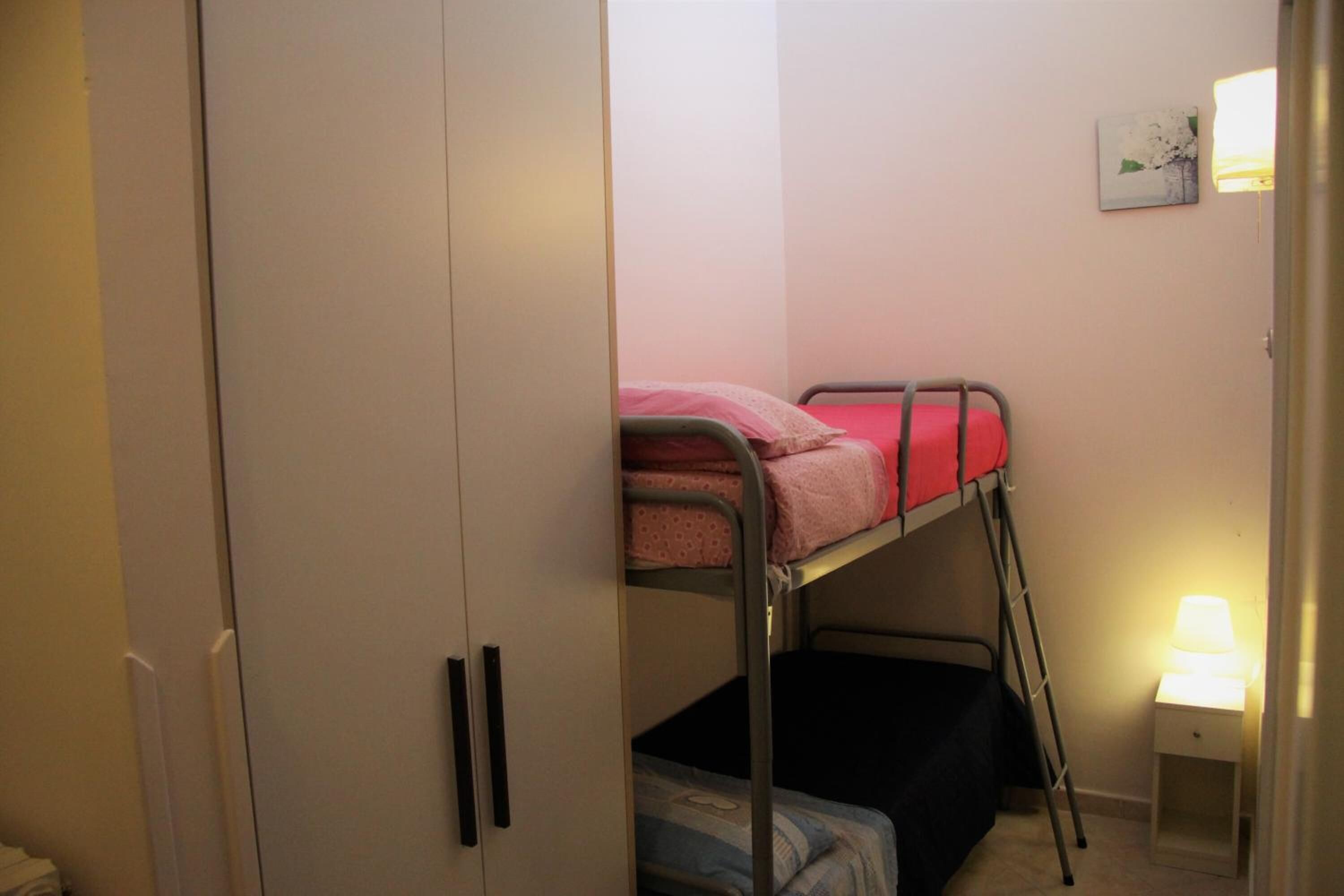 Una cama litera con ropa de cama rosa, una mesita de noche con lámpara y un armario.