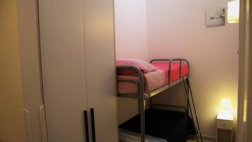 Una cama litera con ropa de cama rosa, una mesita de noche con lámpara y un armario.