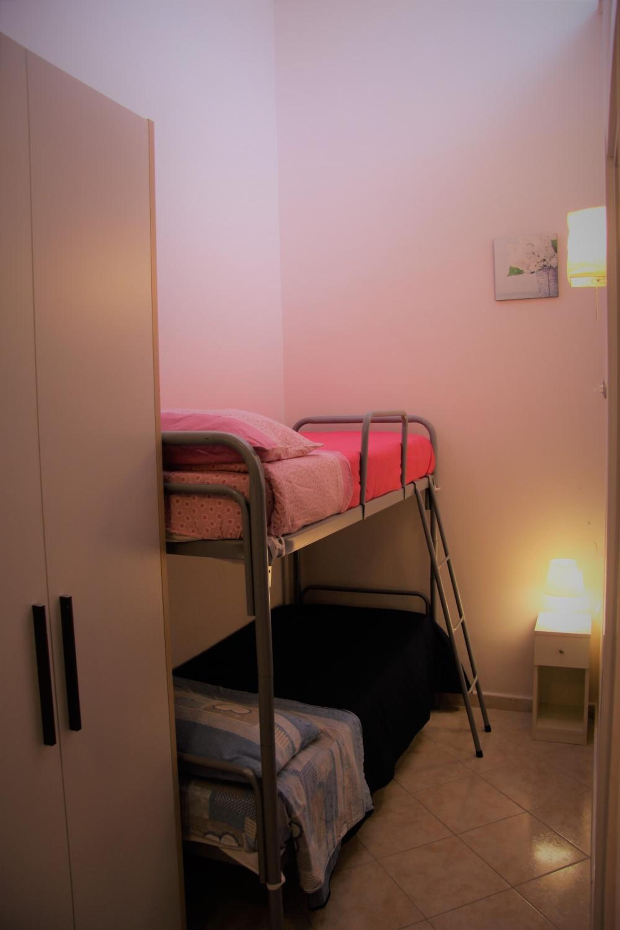 Habitació amb llits superposats, un armari, una taula de nit amb una làmpada i un quadre petit a la paret.