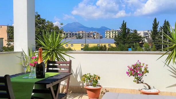 A balcony with a table set for two, a bottle of champagne, and potted plants. - B&B Zefiro (Pompei)
