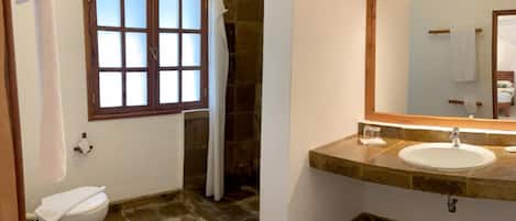 A bathroom with a stone floor, a white sink, a mirror, and a window with frosted glass.