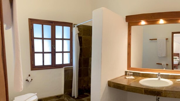 A bathroom with a stone floor, a white sink, a mirror, and a window with frosted glass.