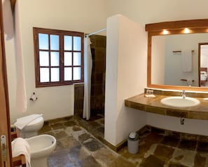 A bathroom with a stone floor, a white sink, a mirror, and a window with frosted glass.
