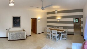 A spacious living area with a dining table, chairs, a ceiling fan, and a wall-mounted light fixture.