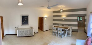 A spacious living area with a dining table, chairs, a ceiling fan, and a wall-mounted light fixture.