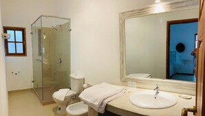 A bathroom with a glass-enclosed shower, a toilet, a sink with a mirror, and a towel on the counter.