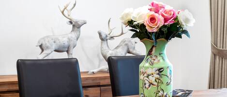 Ein Esstisch mit Blumen in einer Vase, zwei Stühle und zwei Darstellungen von Hirschen an der Wand.