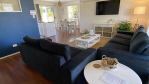 A modern living room with dark sofas, a white coffee table, and a dining area in the background.