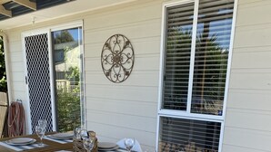 A wooden deck with a dining table set for four, white chairs, and a decorative wall piece.